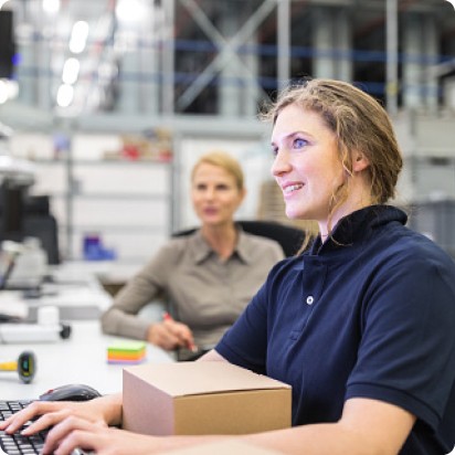 A smiling female employee working on a computer while another looks on at her side.
